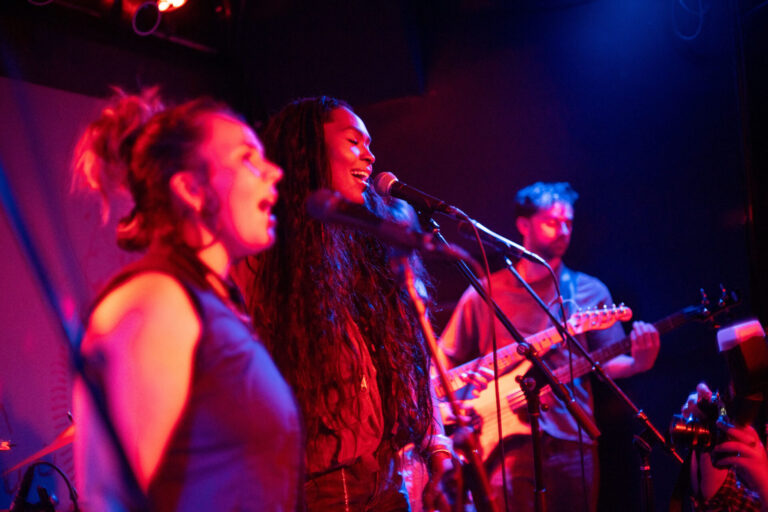 Two backup singers and guitarist in the band Every Us, performing at Pianos NYC in April 2026